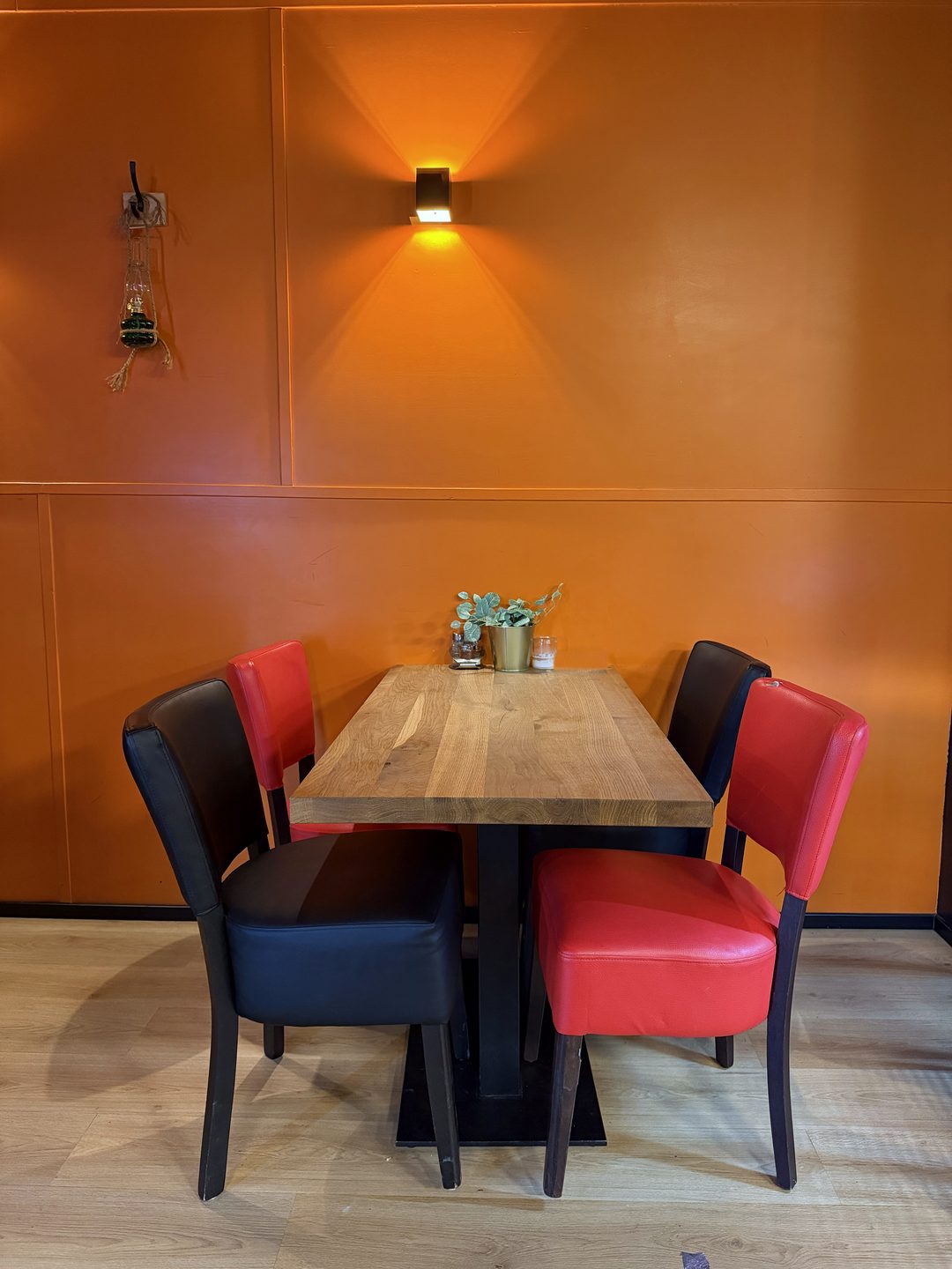 ASPAVA 06: tafel met vier stoelen onder de wandlamp, oranje muur
