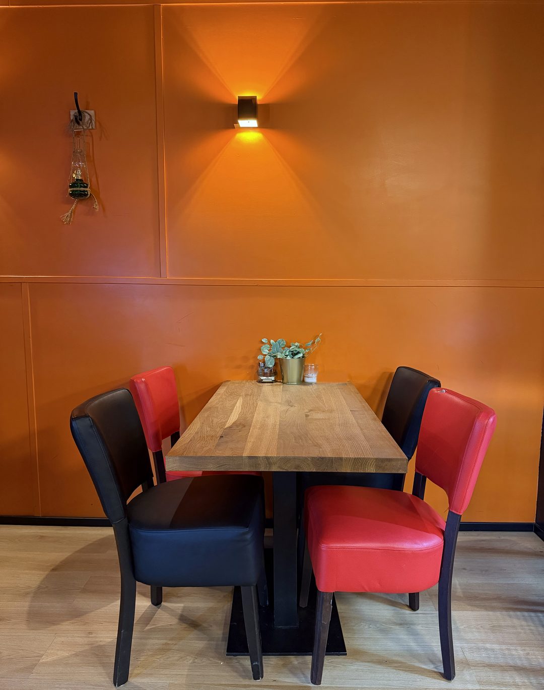 ASPAVA 06: tafel met vier stoelen onder de wandlamp, oranje muur