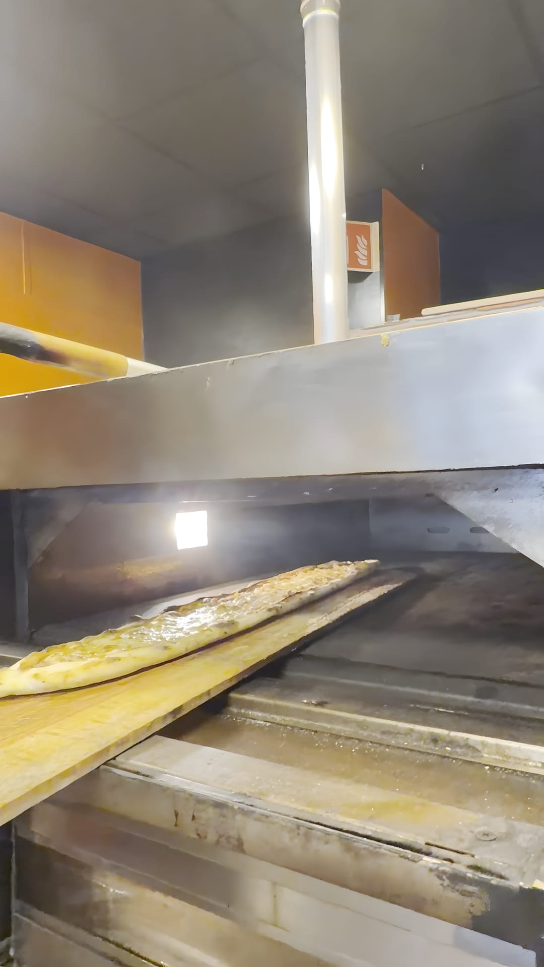 Een lange pide op een houten schep bij de oven